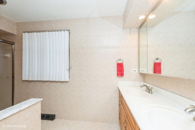 bathroom featuring tile patterned floors, vanity, a shower with shower door, and tile walls