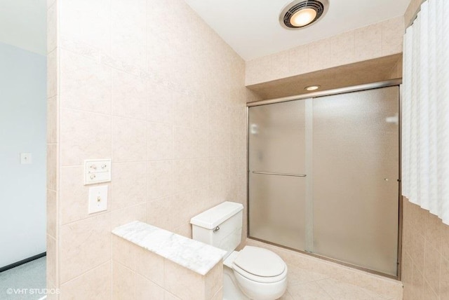 bathroom with toilet, a shower with door, and tile walls