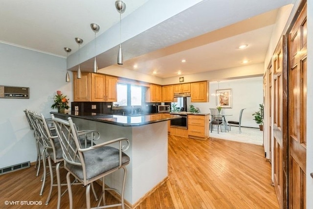 kitchen with kitchen peninsula, decorative backsplash, a kitchen bar, decorative light fixtures, and light hardwood / wood-style flooring