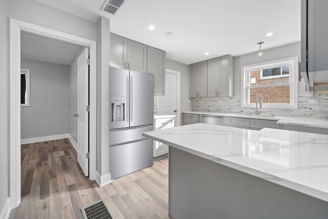 kitchen with backsplash, sink, light hardwood / wood-style flooring, light stone countertops, and appliances with stainless steel finishes