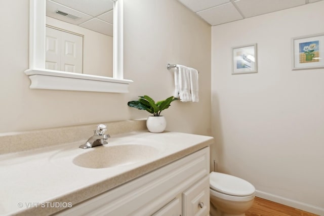 bathroom featuring a drop ceiling, toilet, visible vents, vanity, and baseboards