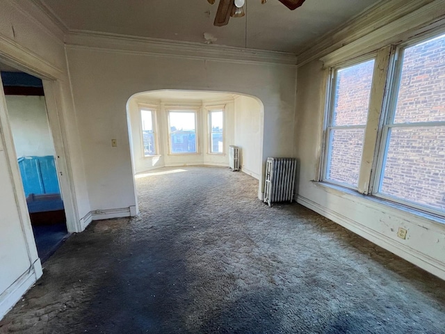 unfurnished living room featuring dark colored carpet, radiator, plenty of natural light, and crown molding