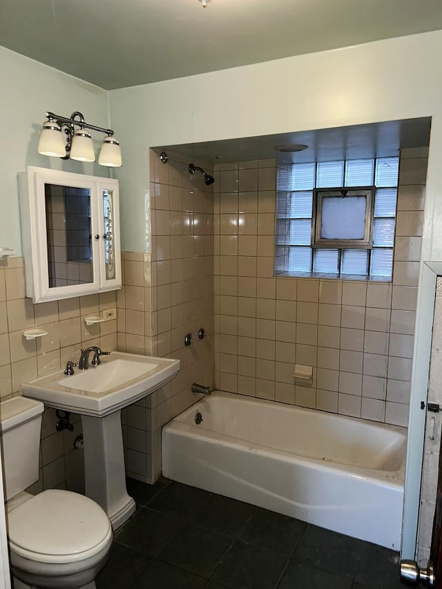 bathroom with tile patterned flooring, tiled shower / bath combo, toilet, and tile walls