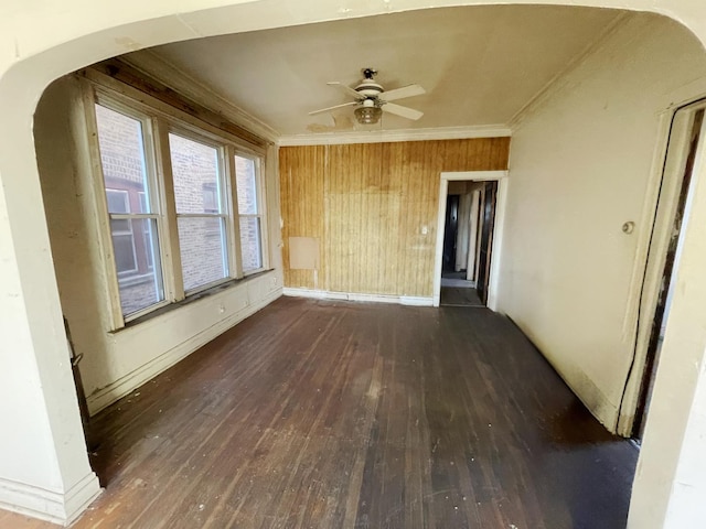 unfurnished room with wooden walls, dark hardwood / wood-style flooring, ceiling fan, and ornamental molding