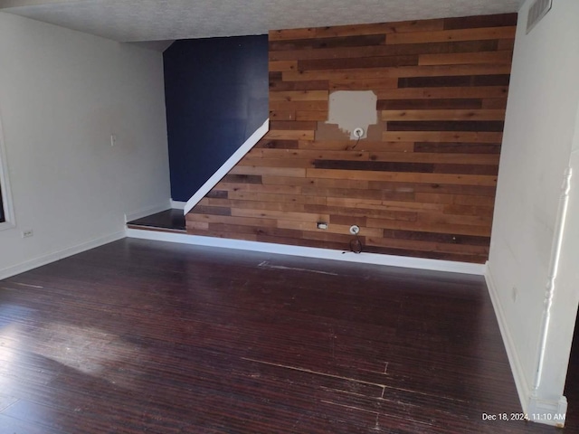 empty room with a textured ceiling, dark hardwood / wood-style floors, and wooden walls