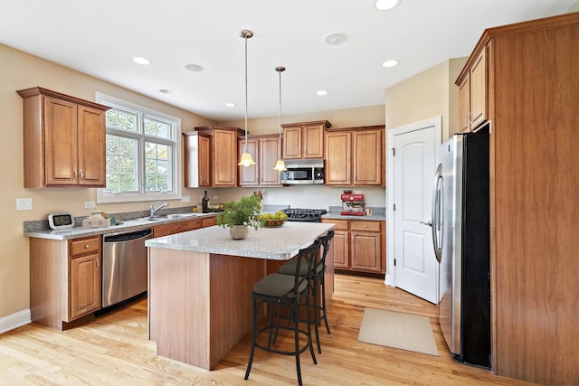 kitchen with hanging light fixtures, a kitchen island, stainless steel appliances, and light hardwood / wood-style floors