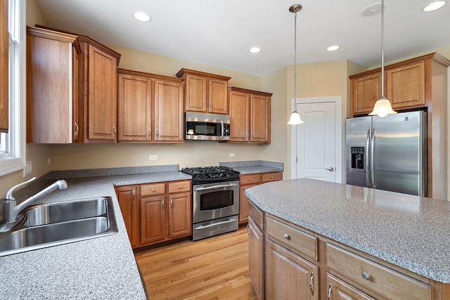 kitchen with hanging light fixtures, sink, a kitchen island, appliances with stainless steel finishes, and light hardwood / wood-style floors