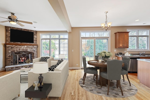 dining area with sink, light hardwood / wood-style floors, ceiling fan with notable chandelier, and a brick fireplace