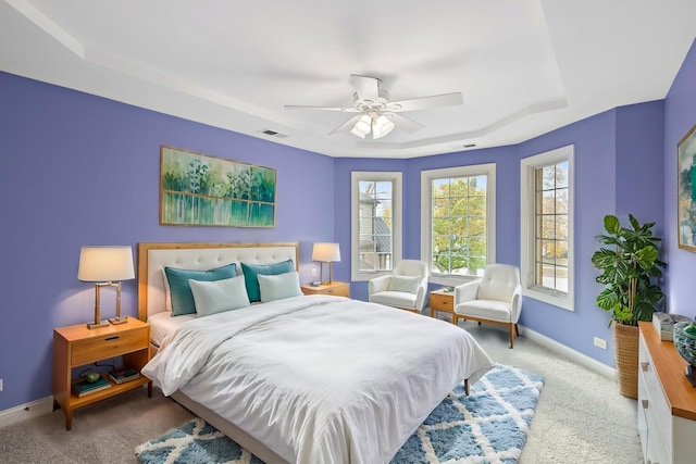 carpeted bedroom with ceiling fan and a tray ceiling