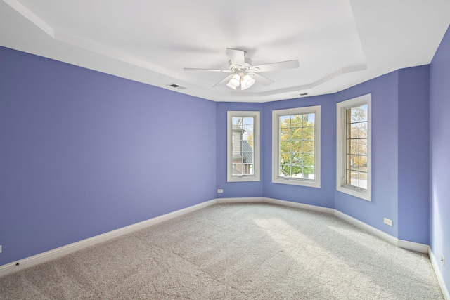 carpeted empty room featuring ceiling fan and a raised ceiling