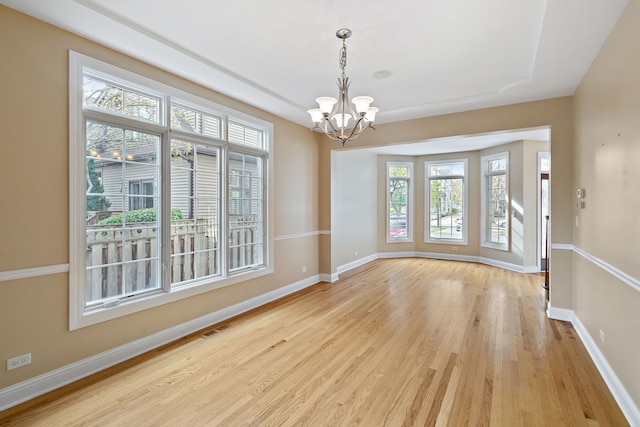 spare room featuring plenty of natural light, light hardwood / wood-style floors, and a chandelier