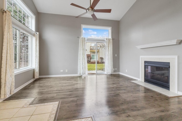 unfurnished living room featuring ceiling fan, a healthy amount of sunlight, light hardwood / wood-style flooring, and a tiled fireplace