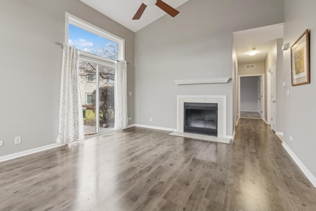 unfurnished living room featuring hardwood / wood-style flooring, ceiling fan, a healthy amount of sunlight, and a tiled fireplace