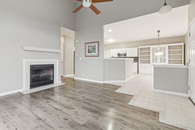 unfurnished living room with a tile fireplace, ceiling fan, light hardwood / wood-style flooring, and a high ceiling