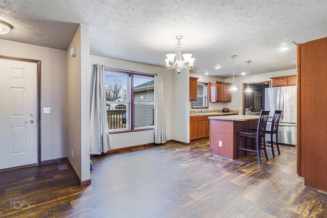 kitchen with a center island, hanging light fixtures, dark hardwood / wood-style floors, stainless steel fridge, and a kitchen bar