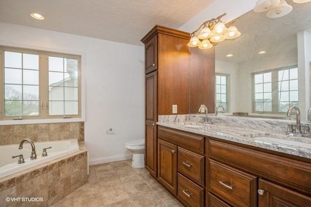 bathroom featuring vanity, tiled tub, toilet, and a wealth of natural light