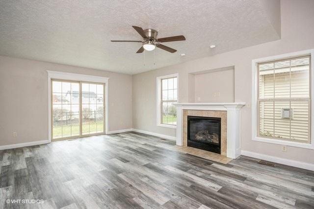 unfurnished living room with a tile fireplace, wood-type flooring, a textured ceiling, and plenty of natural light