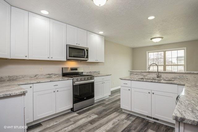 kitchen featuring light stone countertops, appliances with stainless steel finishes, white cabinetry, and sink