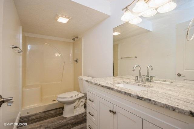 bathroom with vanity, a textured ceiling, a shower, wood-type flooring, and toilet