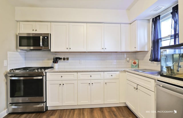 kitchen with white cabinets, light stone countertops, appliances with stainless steel finishes, tasteful backsplash, and dark hardwood / wood-style flooring