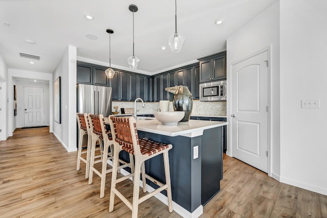 kitchen featuring stainless steel appliances, light hardwood / wood-style floors, decorative light fixtures, a kitchen island with sink, and a breakfast bar