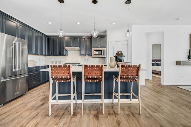 kitchen with a kitchen breakfast bar, backsplash, decorative light fixtures, appliances with stainless steel finishes, and light wood-type flooring