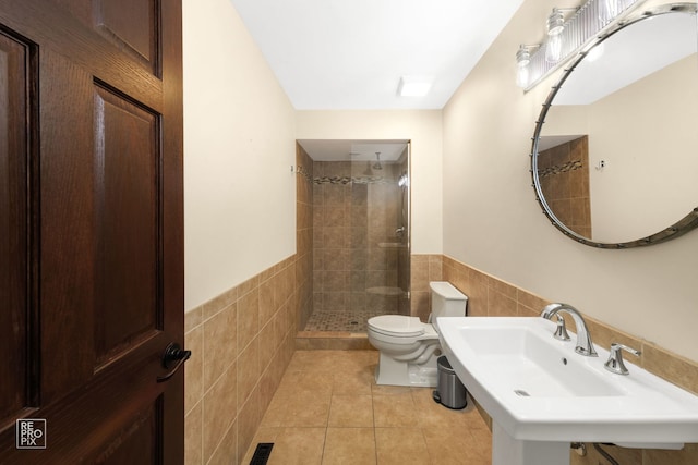 bathroom featuring toilet, a tile shower, tile patterned floors, and tile walls