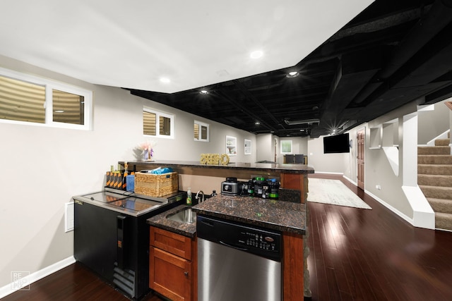 kitchen with dishwasher, sink, dark hardwood / wood-style floors, kitchen peninsula, and dark stone countertops