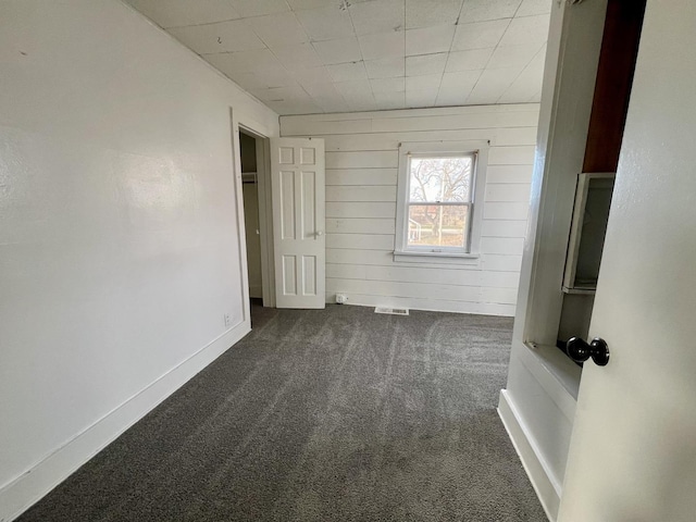 unfurnished bedroom with wooden walls and dark carpet