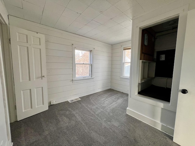 unfurnished bedroom with wooden walls and dark carpet