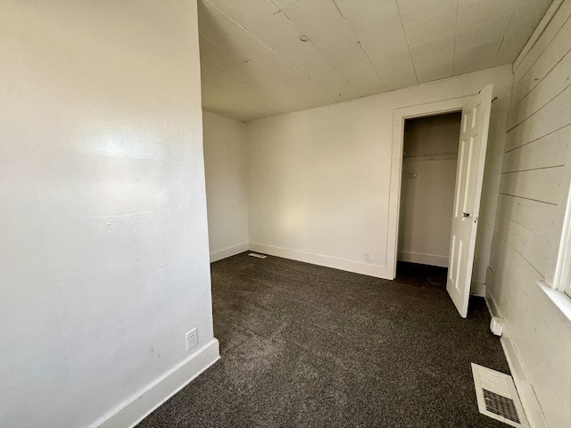 unfurnished bedroom featuring dark carpet, a closet, and wooden walls