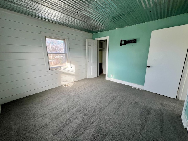 unfurnished bedroom featuring wood walls, dark carpet, and a closet