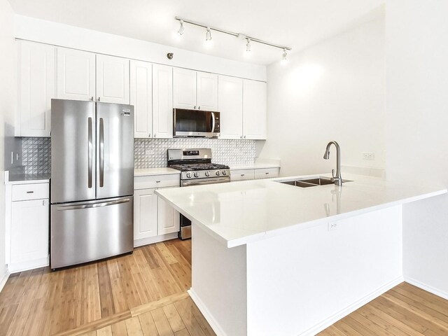 kitchen featuring sink, stainless steel appliances, light hardwood / wood-style flooring, kitchen peninsula, and white cabinets