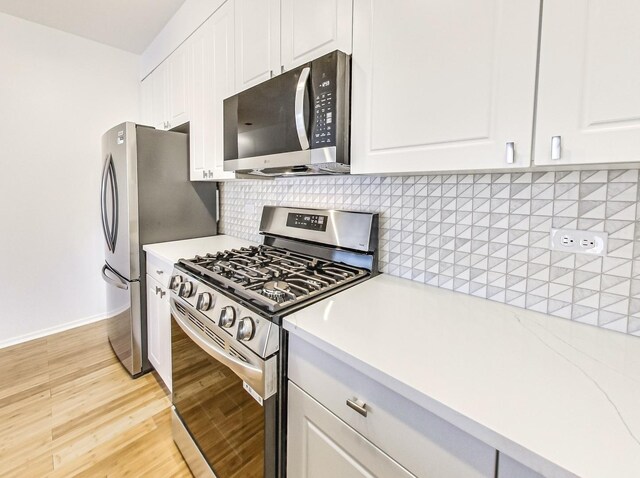 kitchen with white cabinets, appliances with stainless steel finishes, decorative backsplash, and light hardwood / wood-style floors