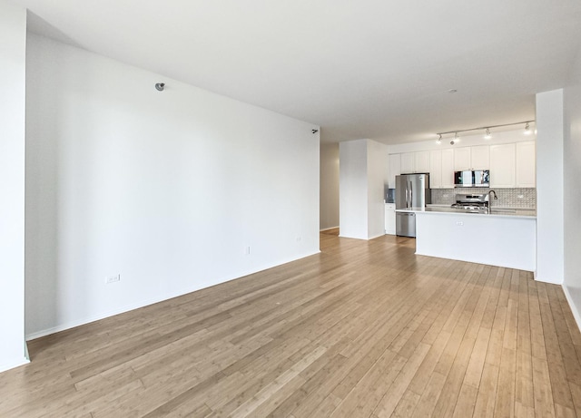 unfurnished living room with rail lighting, sink, and light hardwood / wood-style flooring