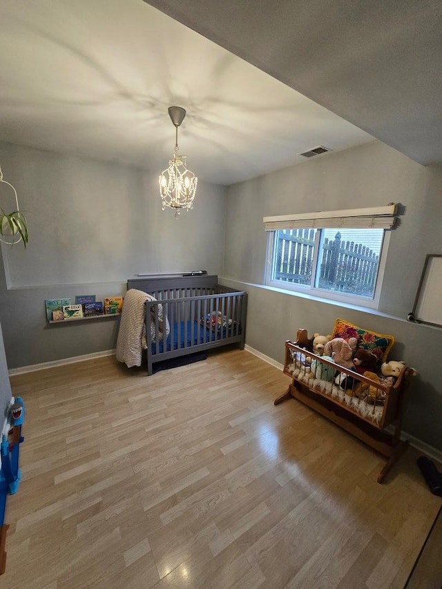 bedroom featuring a chandelier, wood-type flooring, and a nursery area