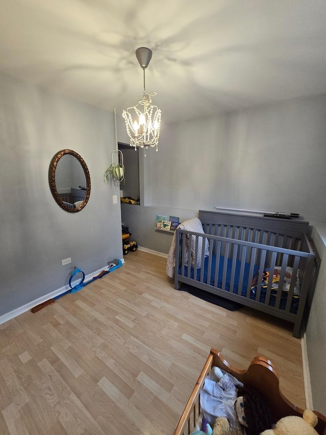 bedroom featuring an inviting chandelier, a crib, and light wood-type flooring