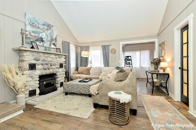 living room featuring wood-type flooring, a wood stove, and vaulted ceiling