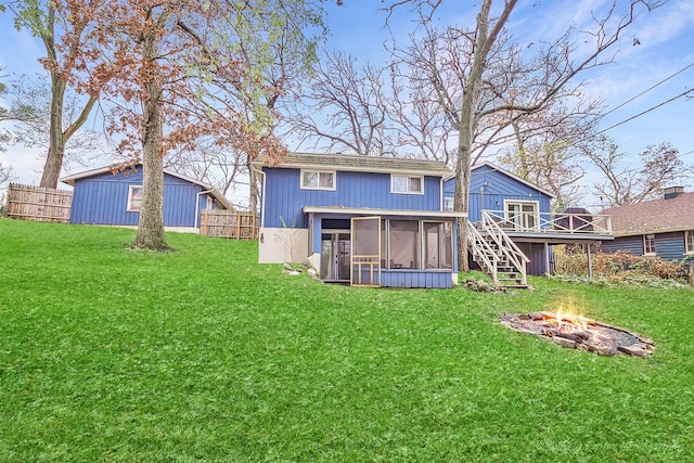 back of property featuring a sunroom, a yard, a deck, and an outdoor fire pit