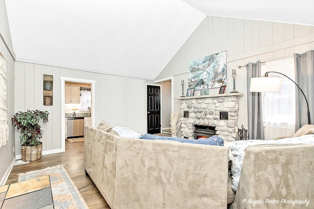 living room featuring vaulted ceiling, a healthy amount of sunlight, wood-type flooring, a stone fireplace, and wood walls