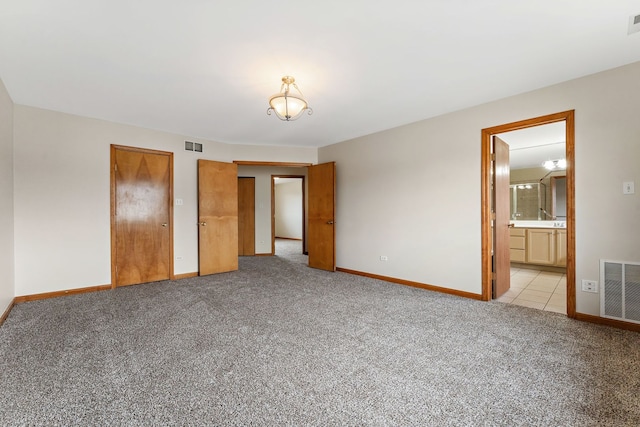 unfurnished bedroom with ensuite bathroom, light carpet, and two closets