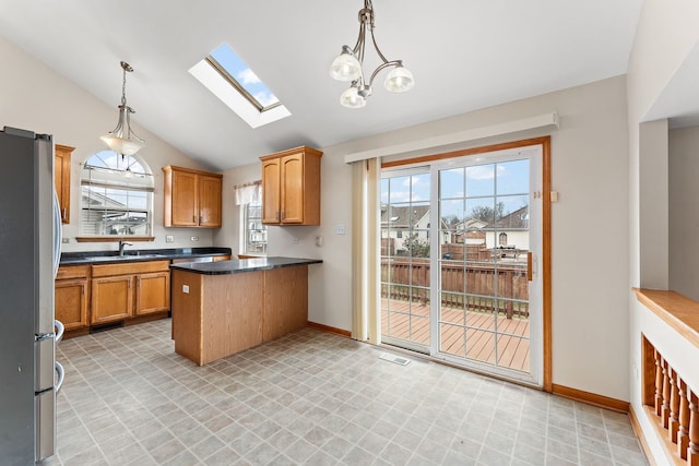 kitchen featuring vaulted ceiling with skylight, sink, hanging light fixtures, and stainless steel refrigerator