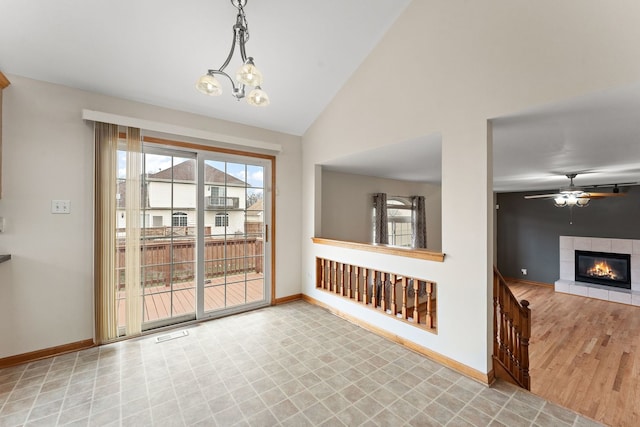 empty room featuring ceiling fan with notable chandelier, vaulted ceiling, light hardwood / wood-style flooring, and a tiled fireplace