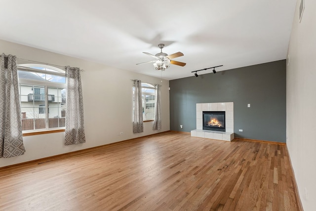 unfurnished living room with track lighting, ceiling fan, a tile fireplace, and light hardwood / wood-style flooring