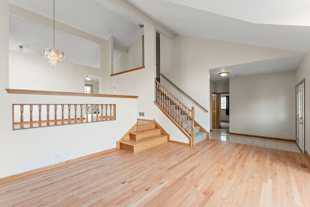 unfurnished living room with hardwood / wood-style flooring, high vaulted ceiling, and an inviting chandelier