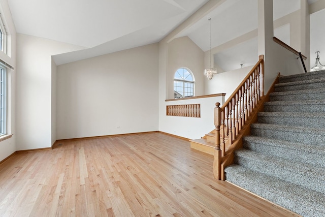 stairs with beamed ceiling, a notable chandelier, wood-type flooring, and high vaulted ceiling