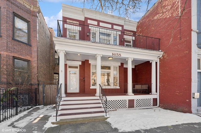 view of front facade with a porch, fence, and brick siding