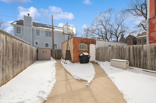 snow covered patio featuring an outbuilding, a storage unit, and a fenced backyard