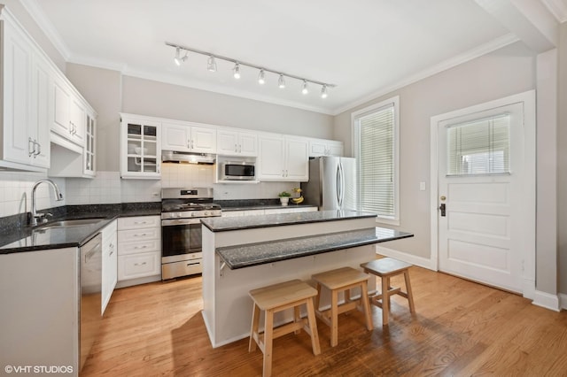 kitchen with under cabinet range hood, ornamental molding, light wood-style flooring, appliances with stainless steel finishes, and a sink