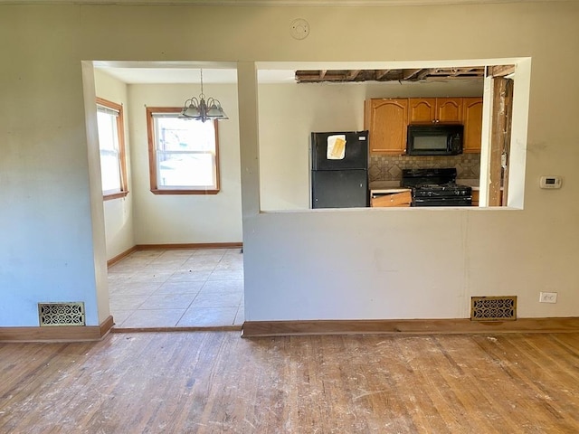 kitchen with tasteful backsplash, black appliances, pendant lighting, an inviting chandelier, and light hardwood / wood-style flooring